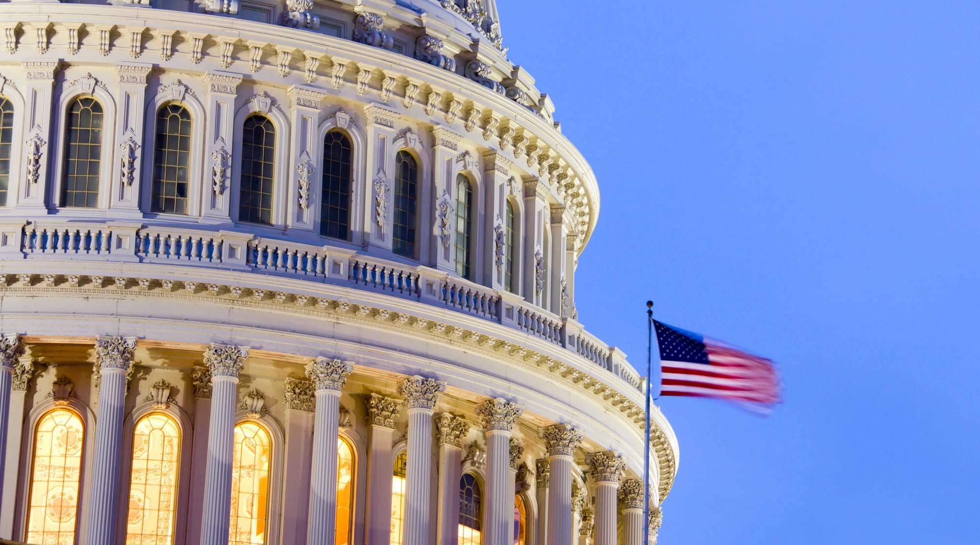 The U.S. Capitol Building's dome at dusk. A U.S. Flag blowing in the wind is slightly blurred by a long exposure speed.